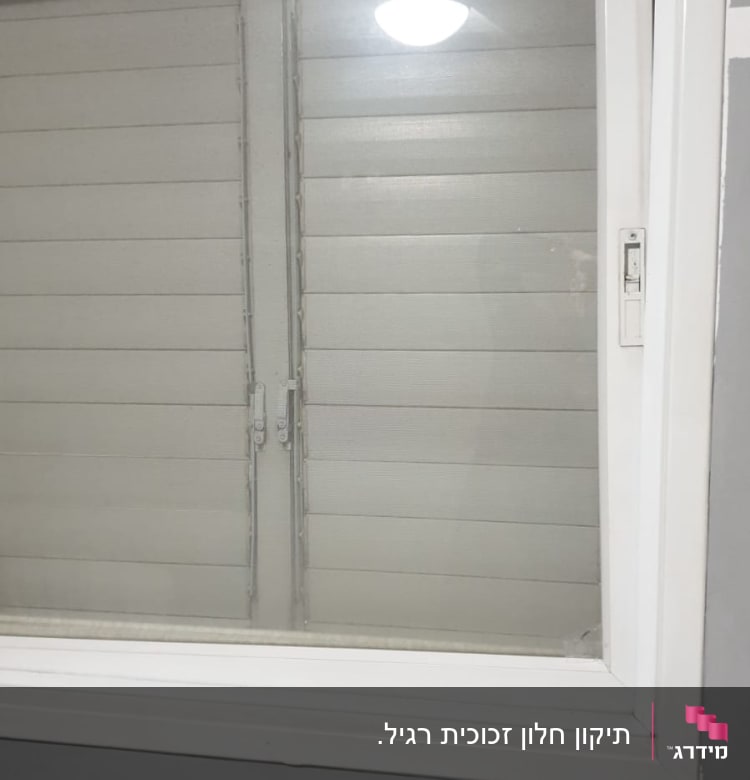 חלון זכוכית עם מסגרת לבנה ותריסים סגורים